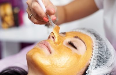 Macro photography of the hand of the beautician with the help of a special brush puts on the face of the girl a golden mask in the spa